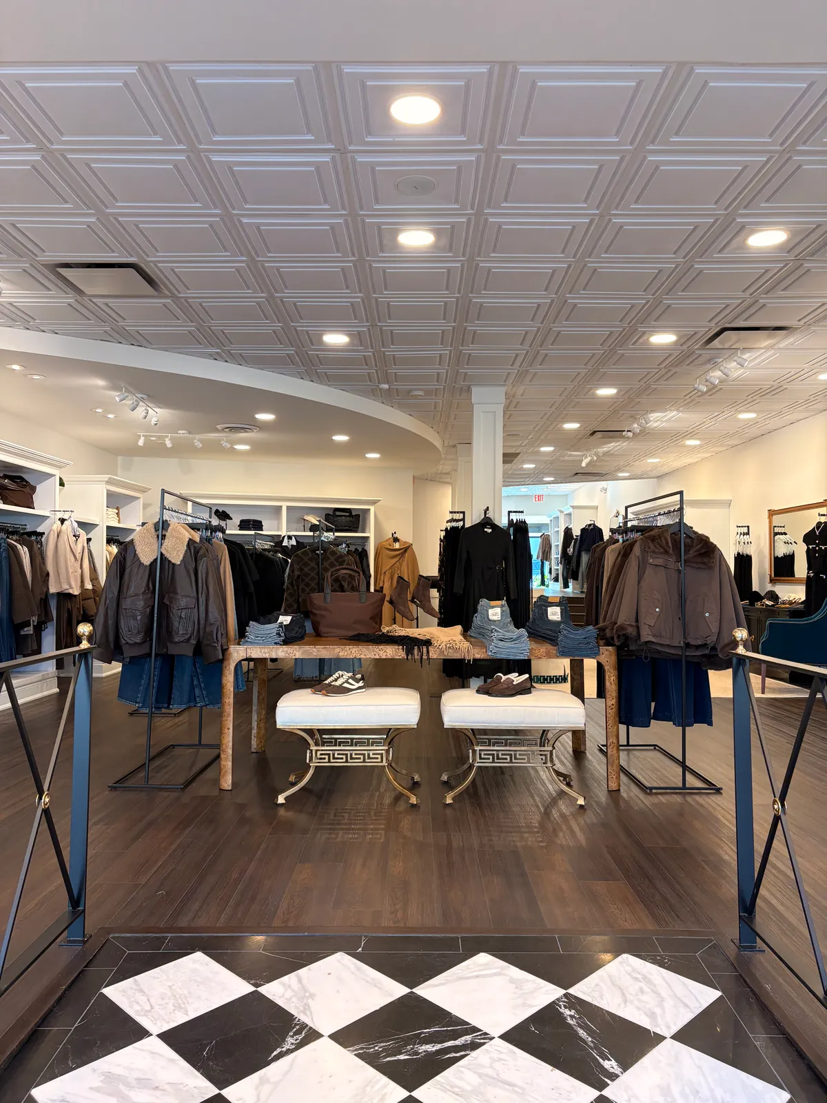 The view in from the marble entry: cream benches at a burl-wood table, racks of jackets and denim beyond