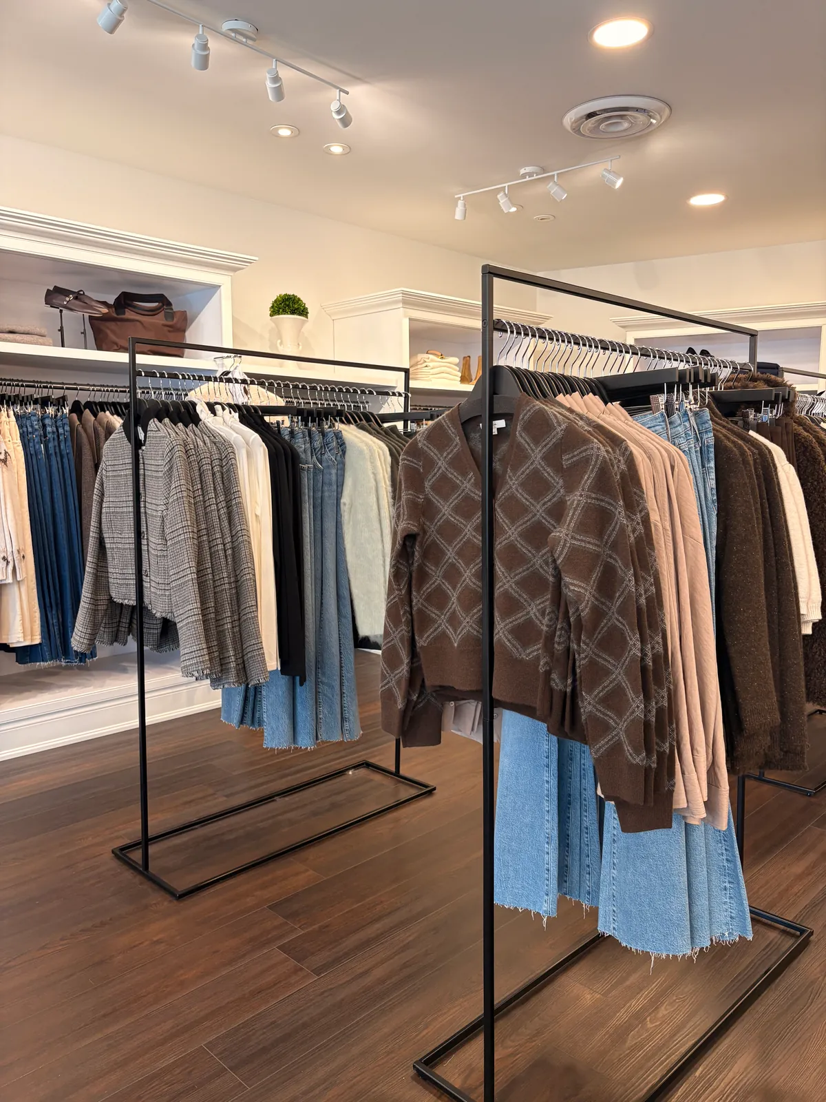 Black rails of plaid jackets, knits and denim on the dark wood floor